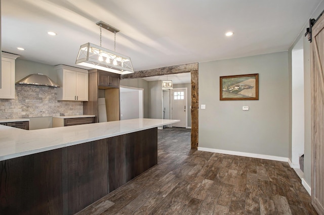 kitchen with light stone countertops, tasteful backsplash, a barn door, dark hardwood / wood-style floors, and pendant lighting