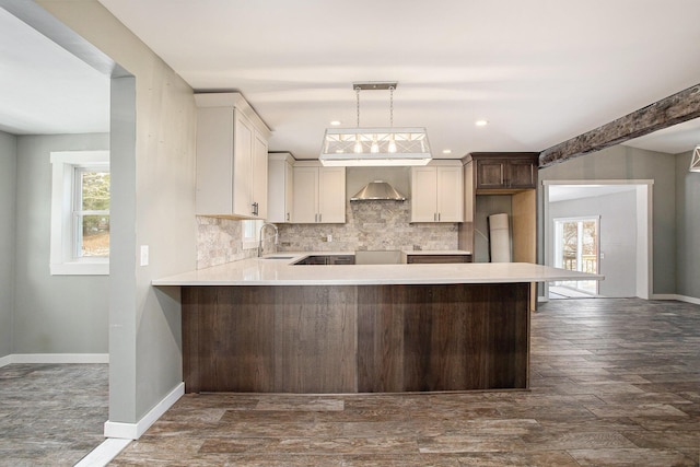 kitchen with sink, wall chimney range hood, tasteful backsplash, kitchen peninsula, and pendant lighting