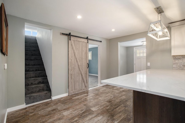 kitchen featuring dark wood-type flooring, a barn door, kitchen peninsula, pendant lighting, and decorative backsplash