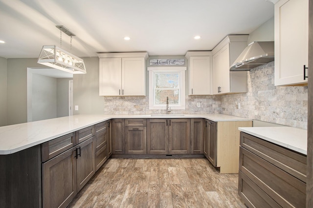 kitchen featuring sink, hanging light fixtures, wall chimney exhaust hood, light hardwood / wood-style floors, and kitchen peninsula