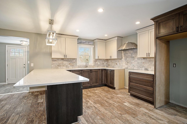 kitchen with wall chimney range hood, sink, hanging light fixtures, light hardwood / wood-style flooring, and tasteful backsplash