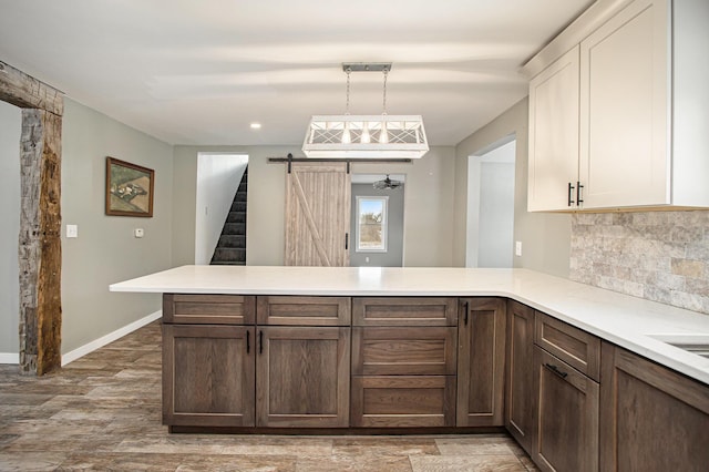 kitchen featuring a barn door, kitchen peninsula, hanging light fixtures, and hardwood / wood-style flooring