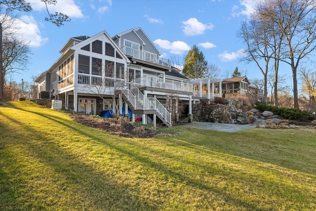 back of house with a sunroom, a wooden deck, and a lawn