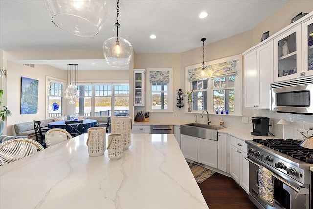 kitchen with pendant lighting, light stone counters, sink, and appliances with stainless steel finishes