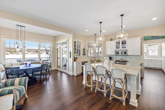 kitchen with a kitchen bar, backsplash, white cabinetry, and hanging light fixtures