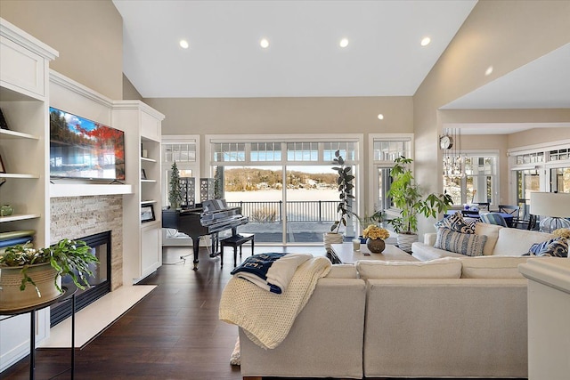 living room featuring built in shelves, a healthy amount of sunlight, a stone fireplace, and dark wood-type flooring