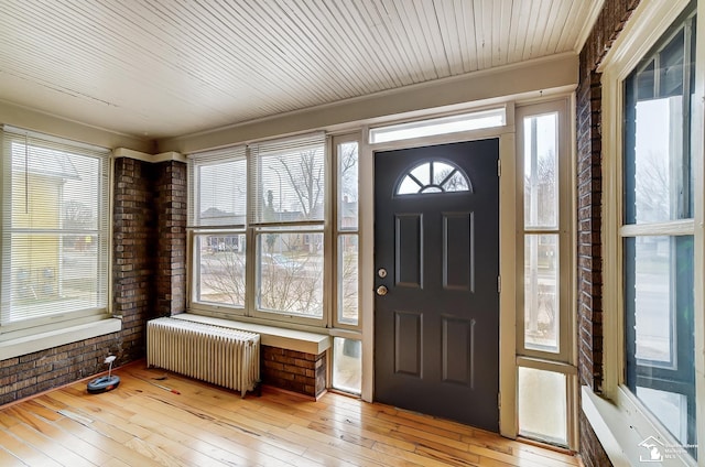 entrance foyer with plenty of natural light, radiator heating unit, brick wall, and light hardwood / wood-style flooring