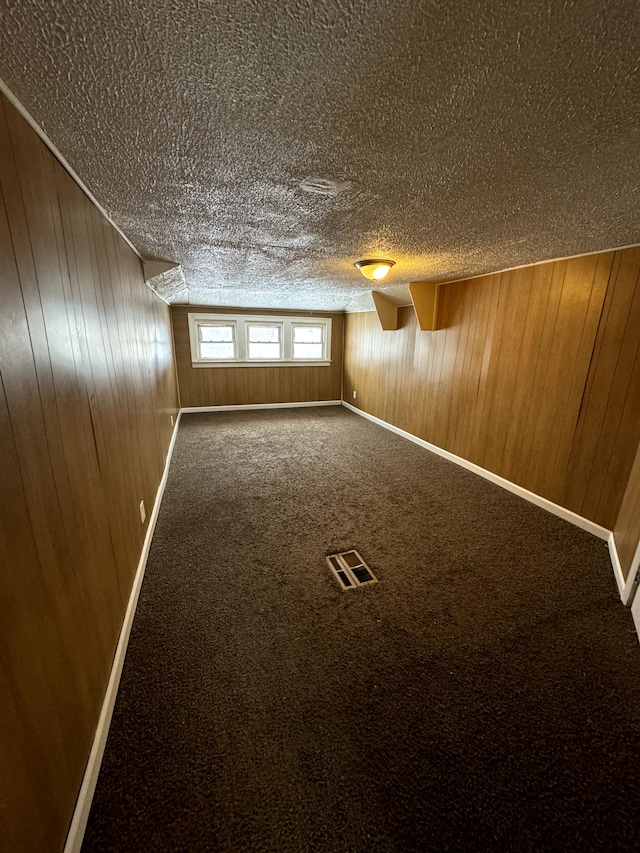 interior space featuring carpet, a textured ceiling, and wood walls