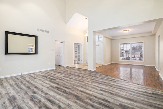 unfurnished living room featuring a high ceiling, visible vents, baseboards, and wood finished floors