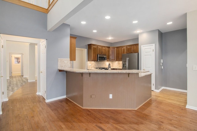 kitchen featuring decorative backsplash, appliances with stainless steel finishes, a peninsula, light wood-type flooring, and a kitchen bar