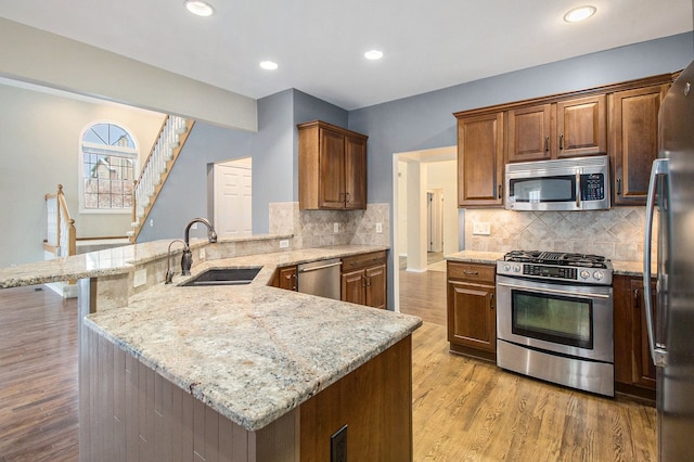 kitchen with light wood finished floors, a peninsula, light stone countertops, stainless steel appliances, and a sink