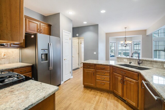 kitchen featuring backsplash, sink, appliances with stainless steel finishes, light stone countertops, and a chandelier