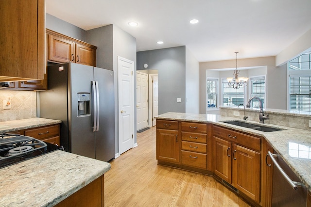 kitchen featuring stainless steel appliances, a sink, light wood-style floors, light stone countertops, and brown cabinetry