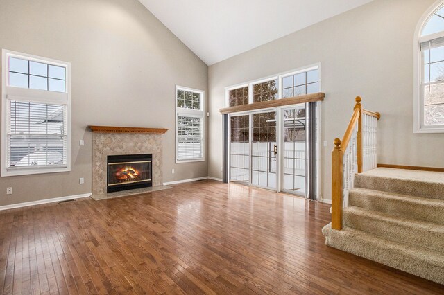 unfurnished living room with high vaulted ceiling, a tiled fireplace, plenty of natural light, and hardwood / wood-style floors