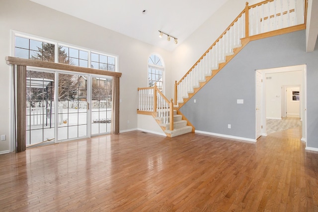 unfurnished living room with stairway, wood finished floors, a towering ceiling, and baseboards