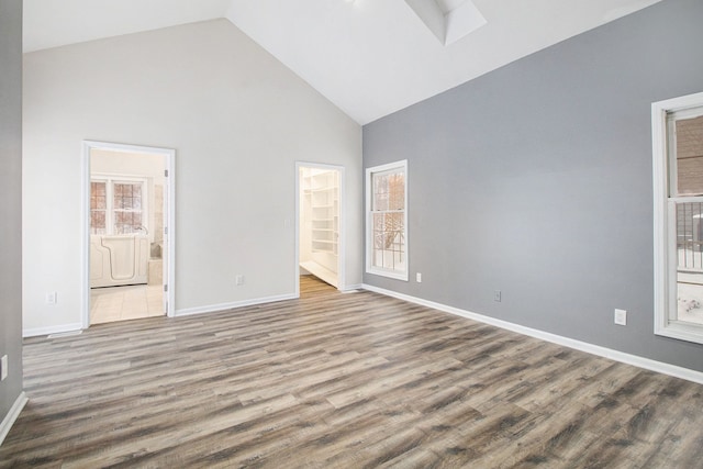 unfurnished room with high vaulted ceiling, washer / clothes dryer, baseboards, and wood finished floors