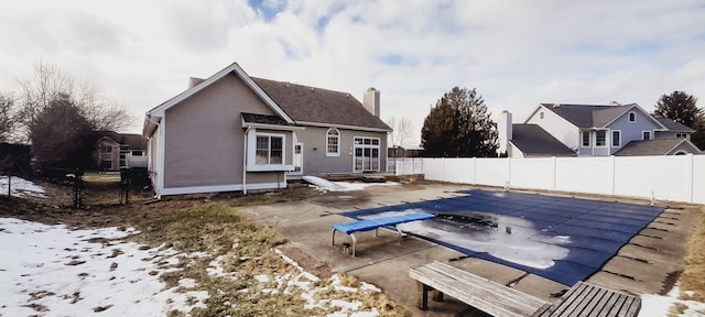 rear view of property featuring a fenced in pool, a patio area, a fenced backyard, and a chimney