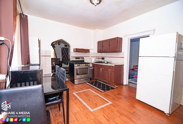 kitchen with decorative backsplash, light hardwood / wood-style flooring, white fridge, and gas stove