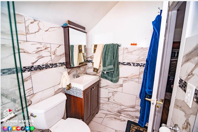 bathroom with tile walls, toilet, vanity, and lofted ceiling