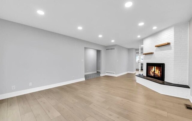 unfurnished living room featuring light wood-type flooring and a brick fireplace