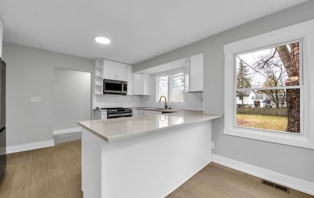 kitchen featuring white cabinets, sink, appliances with stainless steel finishes, light hardwood / wood-style floors, and kitchen peninsula