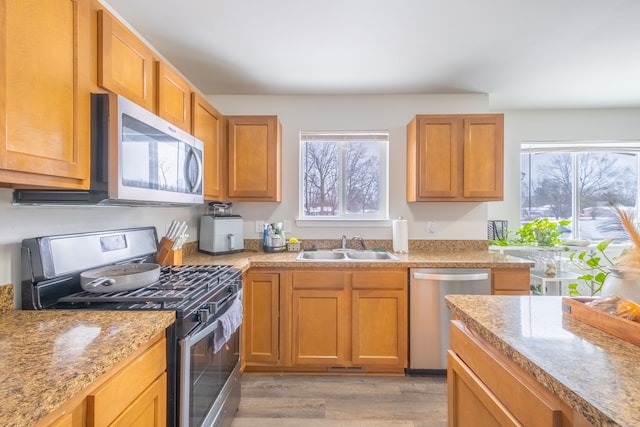 kitchen featuring light wood finished floors, light countertops, brown cabinets, appliances with stainless steel finishes, and a sink