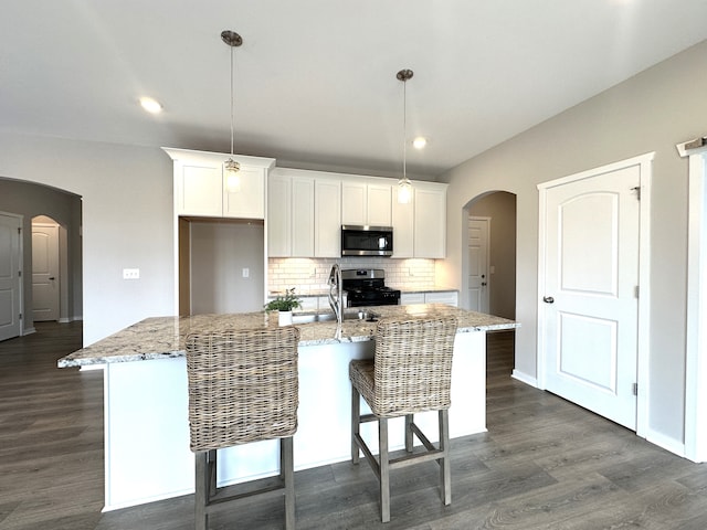 kitchen with white cabinets, pendant lighting, stainless steel appliances, and an island with sink