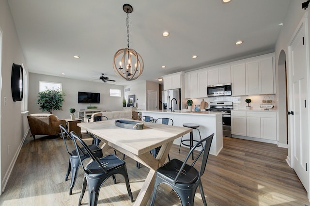 dining area with sink, dark hardwood / wood-style floors, and ceiling fan with notable chandelier