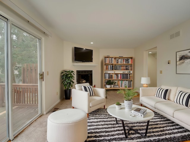 living room featuring baseboards, a fireplace, visible vents, and light colored carpet