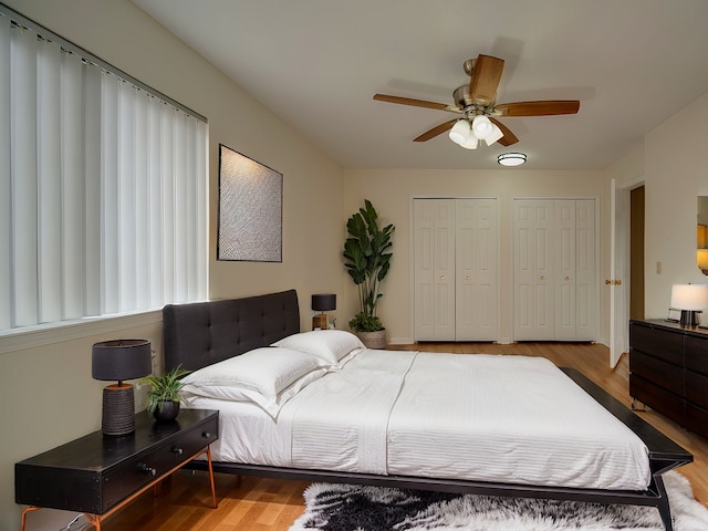 bedroom featuring a ceiling fan, multiple closets, and wood finished floors