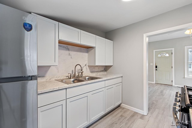 kitchen featuring stove, white cabinets, sink, light hardwood / wood-style floors, and stainless steel refrigerator