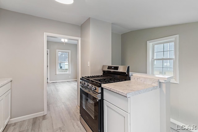 kitchen with stainless steel gas range oven, white cabinetry, vaulted ceiling, and a wealth of natural light