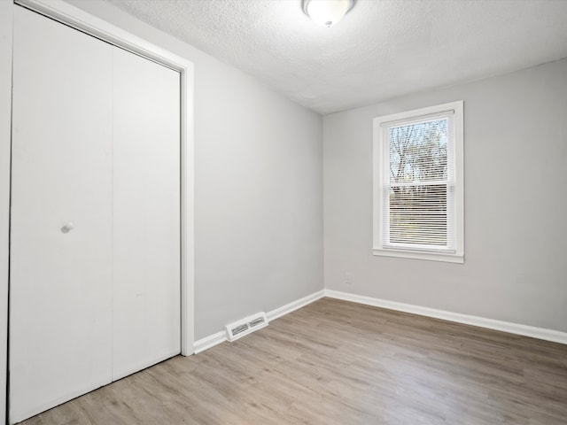 unfurnished bedroom featuring a closet, a textured ceiling, and light hardwood / wood-style flooring