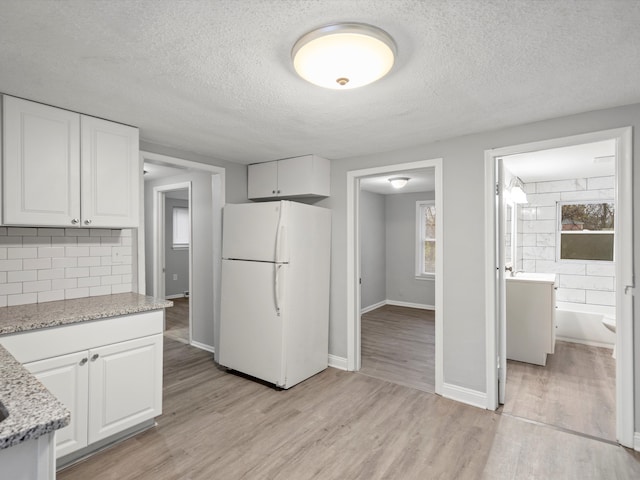 kitchen featuring white refrigerator, light stone countertops, white cabinetry, and a healthy amount of sunlight