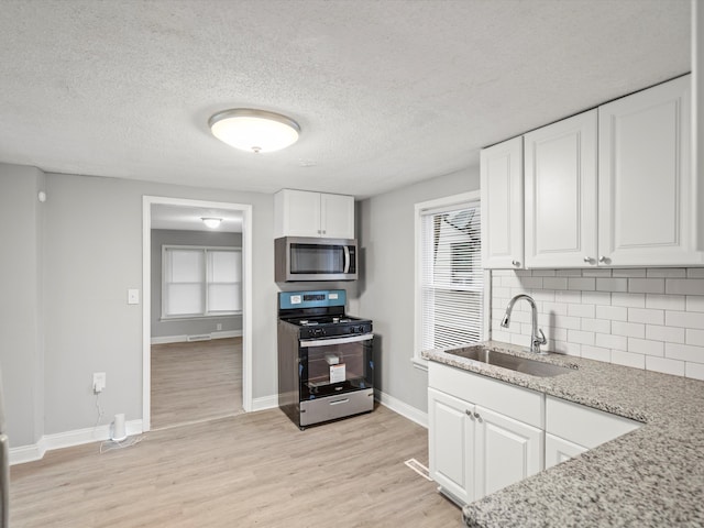 kitchen with backsplash, white cabinets, sink, light stone countertops, and stainless steel appliances