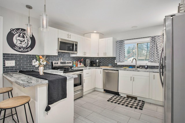 kitchen featuring stainless steel appliances, light stone countertops, white cabinets, and decorative light fixtures