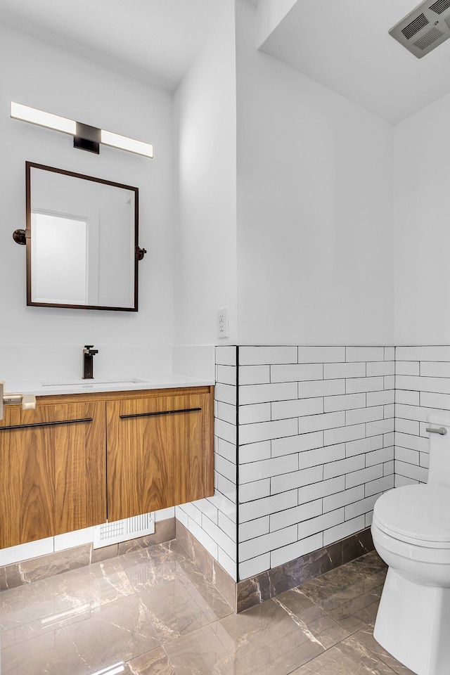 bathroom with vanity, toilet, and tile walls