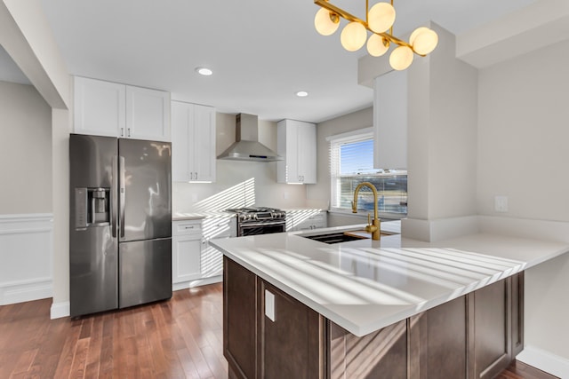 kitchen with kitchen peninsula, appliances with stainless steel finishes, sink, wall chimney range hood, and white cabinetry