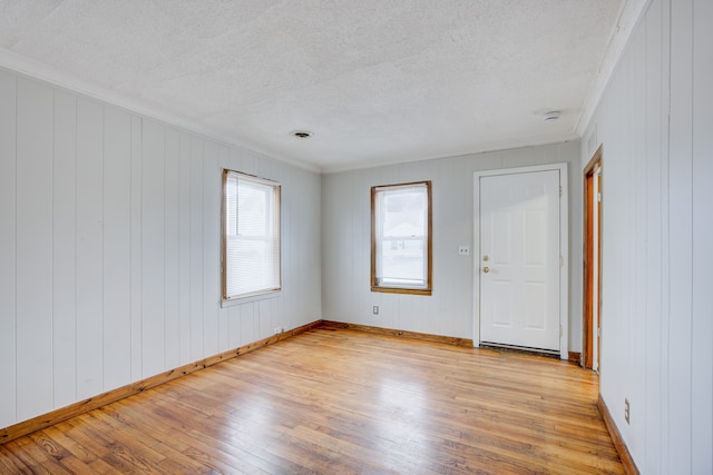 spare room with a textured ceiling, light wood-type flooring, wooden walls, and ornamental molding