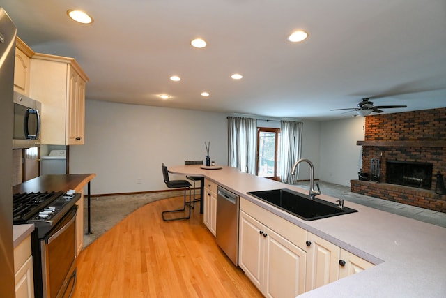 kitchen featuring ceiling fan, a fireplace, washer / dryer, sink, and stainless steel appliances