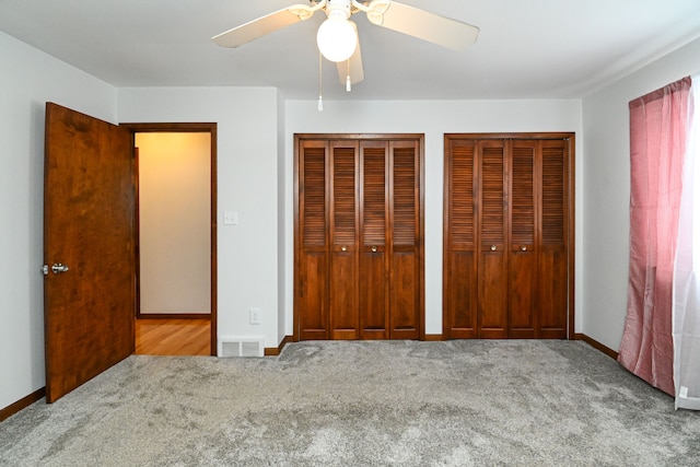 unfurnished bedroom featuring ceiling fan, light colored carpet, and two closets