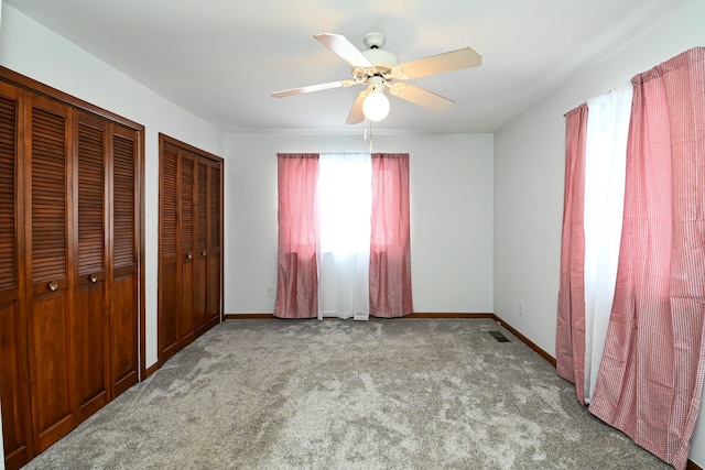 unfurnished bedroom featuring ceiling fan, two closets, and light colored carpet