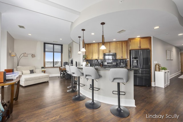 kitchen with appliances with stainless steel finishes, tasteful backsplash, hanging light fixtures, and dark wood-type flooring