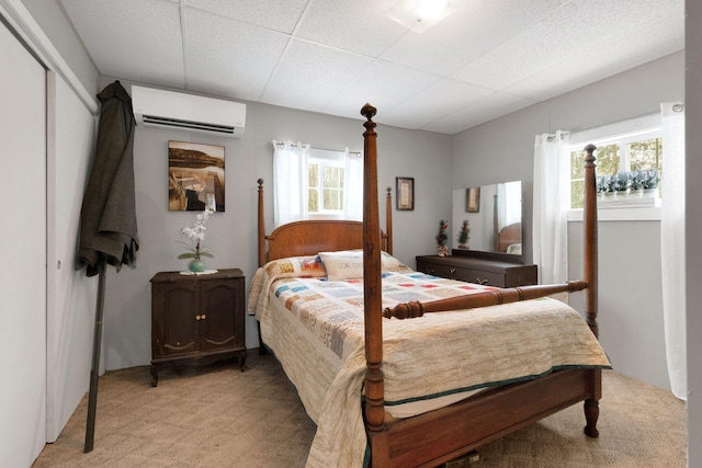 bedroom with a wall unit AC, a paneled ceiling, a closet, and light colored carpet