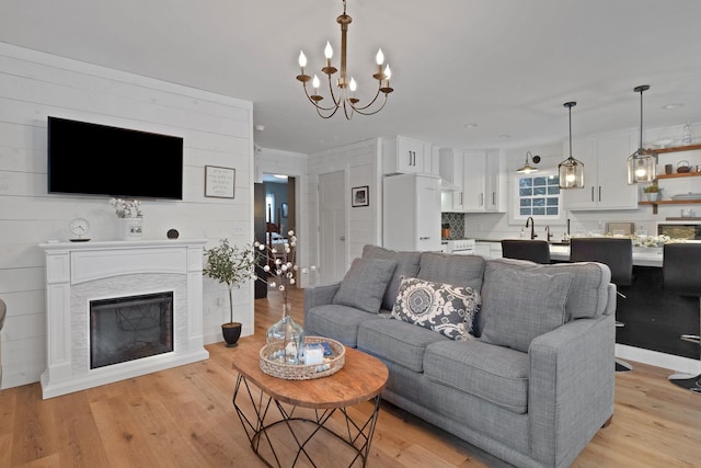 living room featuring a stone fireplace, light hardwood / wood-style flooring, and a chandelier