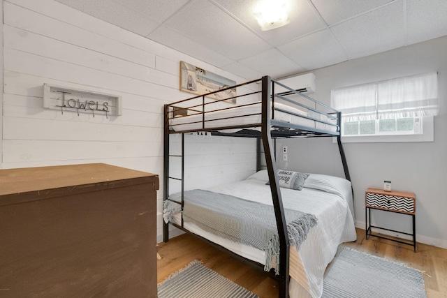 bedroom with wooden walls, a drop ceiling, hardwood / wood-style floors, and a wall mounted air conditioner