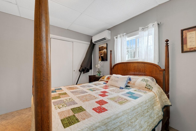 carpeted bedroom with a paneled ceiling, an AC wall unit, and a closet