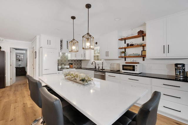 kitchen featuring a center island, decorative light fixtures, white appliances, a breakfast bar area, and white cabinets