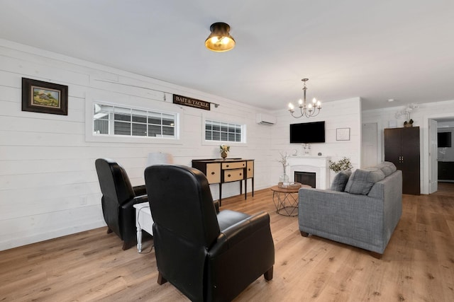 living room featuring light wood-type flooring, an inviting chandelier, a wall mounted AC, and wooden walls