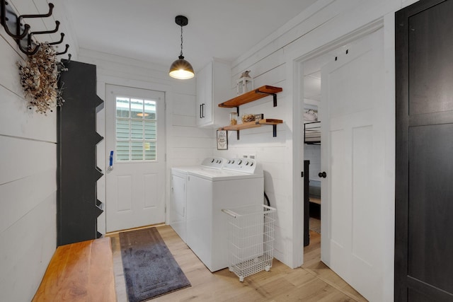 clothes washing area with cabinets, washing machine and dryer, and light wood-type flooring